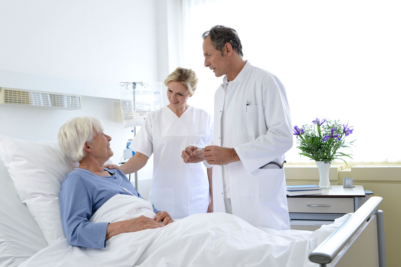 Ärzteteam spricht mit älterer Patientin im Krankenhausbett.