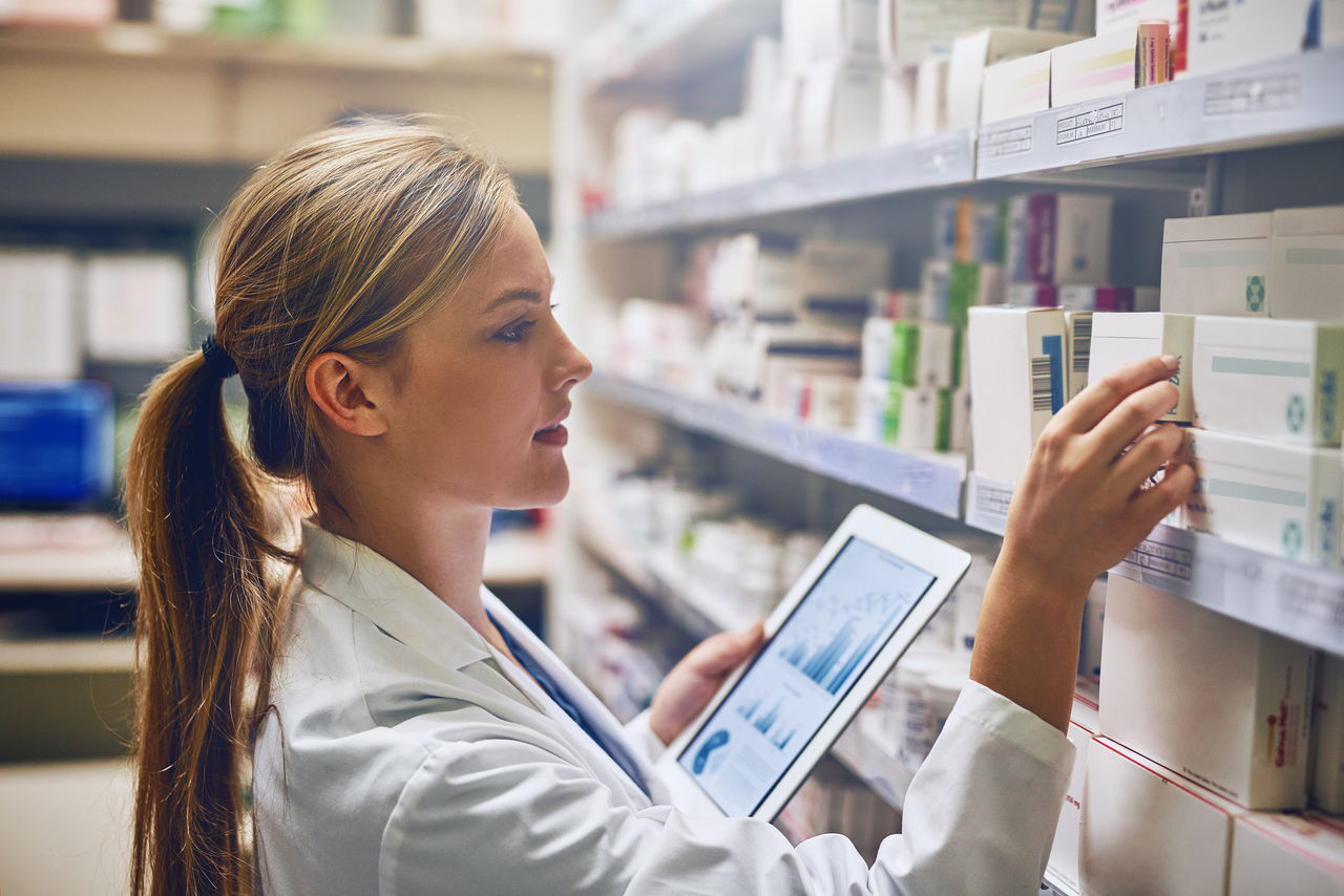 Pharmacienne consultant une tablette et organisant des médicaments en pharmacie.
